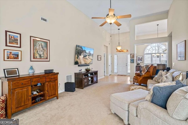 living room with light colored carpet, ceiling fan with notable chandelier, a high ceiling, visible vents, and baseboards