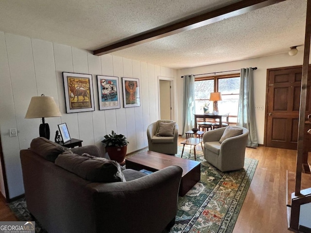 living area with a textured ceiling, light wood finished floors, and beamed ceiling