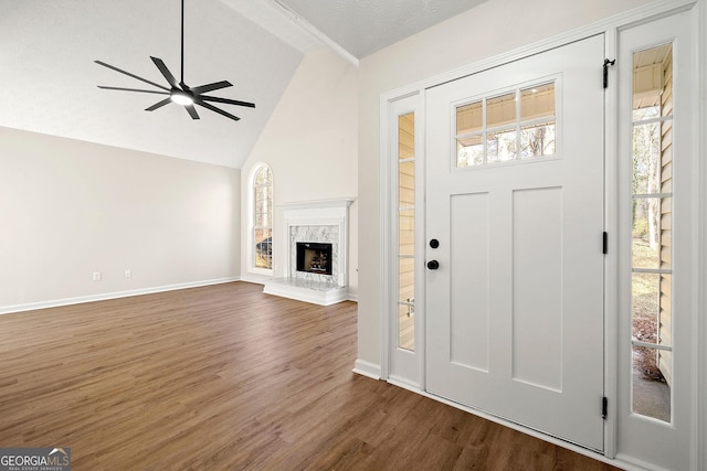 foyer entrance with a high end fireplace, dark wood-style flooring, vaulted ceiling, and ceiling fan