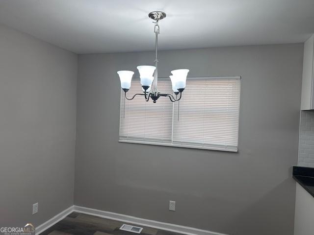 unfurnished dining area with visible vents, dark wood finished floors, a notable chandelier, and baseboards