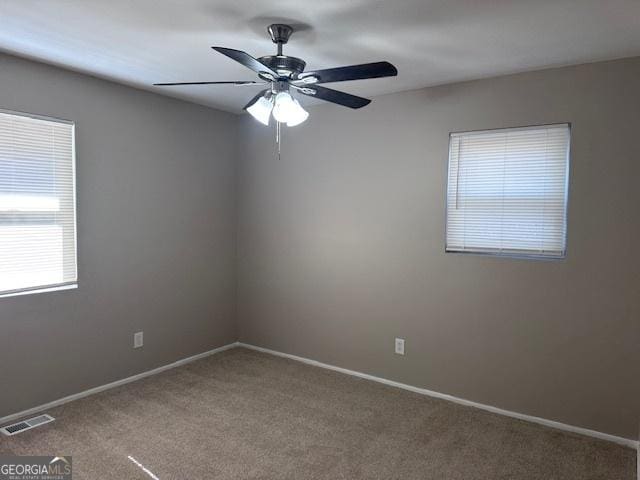 carpeted empty room featuring baseboards, visible vents, and ceiling fan