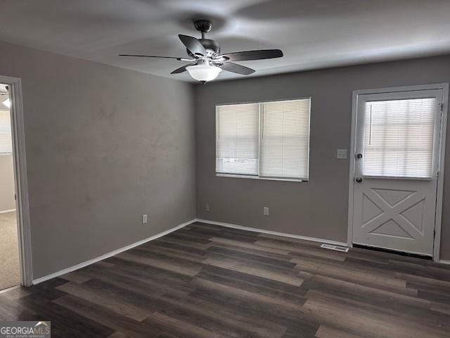 interior space with ceiling fan, visible vents, baseboards, and dark wood finished floors