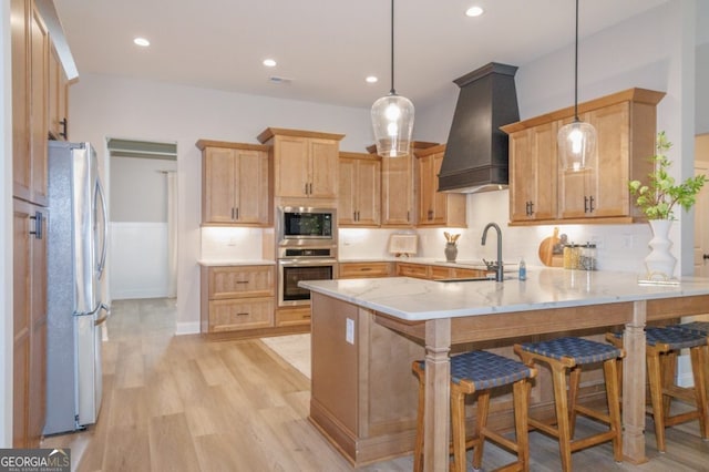 kitchen featuring a breakfast bar area, appliances with stainless steel finishes, a peninsula, hanging light fixtures, and premium range hood