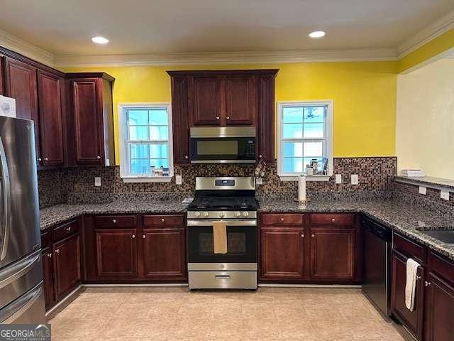 kitchen featuring reddish brown cabinets, appliances with stainless steel finishes, dark stone countertops, and a healthy amount of sunlight