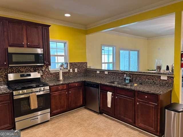 kitchen with a sink, a peninsula, appliances with stainless steel finishes, and dark stone countertops