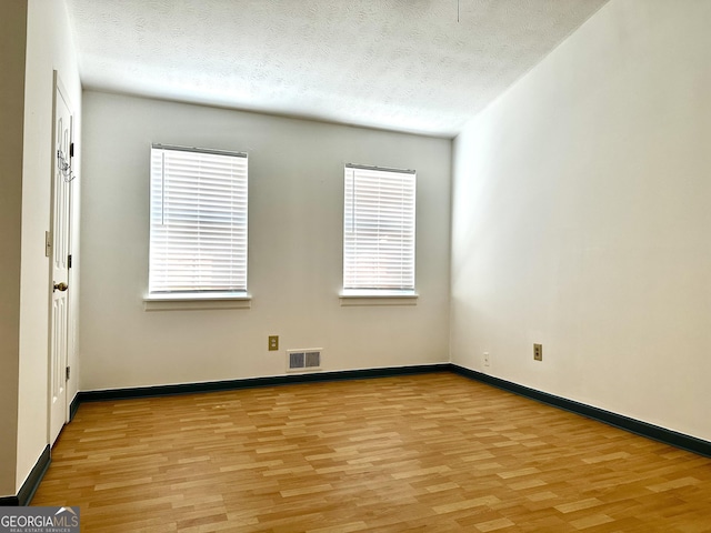 empty room with visible vents, a textured ceiling, and light wood finished floors