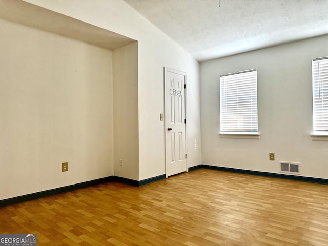 empty room with visible vents, a textured ceiling, baseboards, and wood finished floors