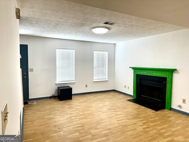 unfurnished living room with light wood finished floors, visible vents, baseboards, a fireplace with flush hearth, and a textured ceiling