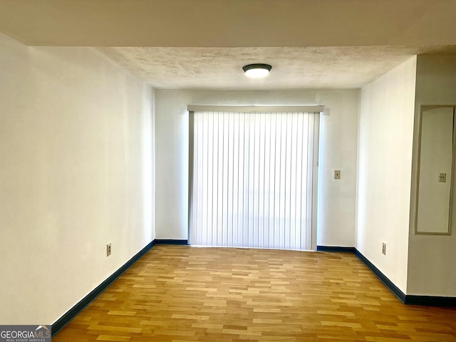 unfurnished room featuring light wood-style flooring, a textured ceiling, and baseboards