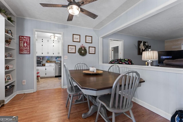 dining area with a textured ceiling, ceiling fan, ornamental molding, and light wood-type flooring