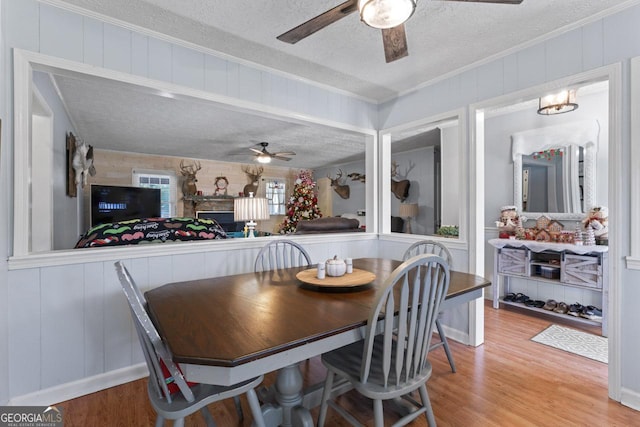 dining space featuring a ceiling fan, ornamental molding, a textured ceiling, and wood finished floors