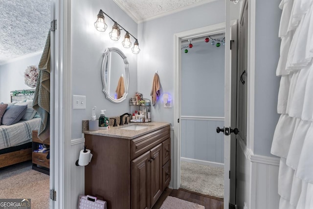 ensuite bathroom with a textured ceiling, connected bathroom, a wainscoted wall, vanity, and crown molding