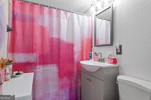 bathroom with a shower with shower curtain, toilet, a textured ceiling, vanity, and tile walls