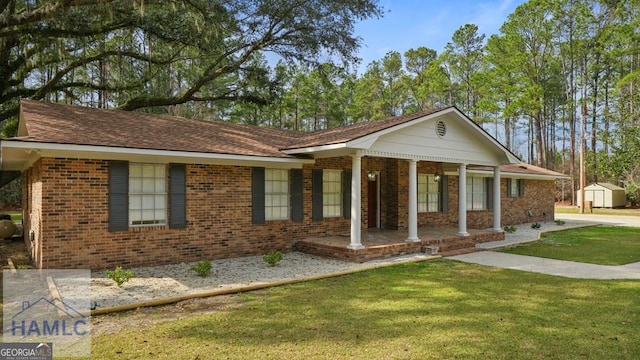 ranch-style home with a front yard, covered porch, brick siding, and a shed