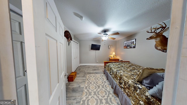 bedroom with a textured ceiling, ceiling fan, light wood-type flooring, and baseboards