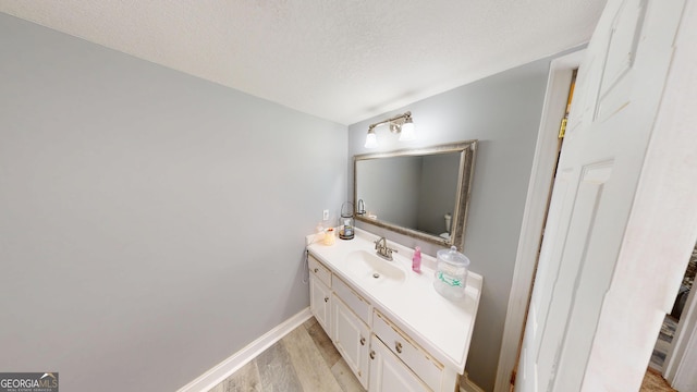 bathroom featuring a textured ceiling, baseboards, wood finished floors, and vanity