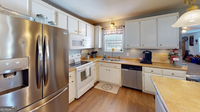 kitchen with hanging light fixtures, stainless steel appliances, light countertops, white cabinetry, and a sink