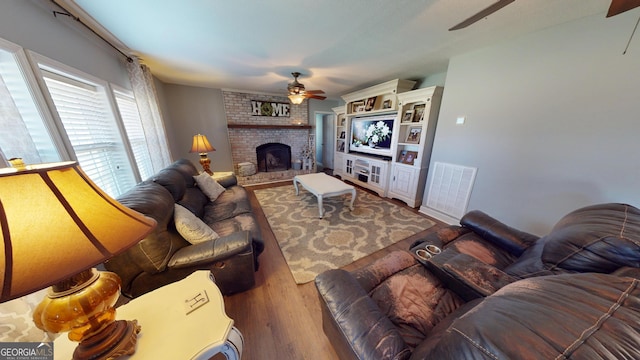 living room featuring a fireplace, visible vents, a ceiling fan, and wood finished floors