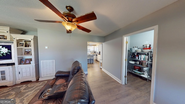 living area with visible vents, a ceiling fan, a textured ceiling, wood finished floors, and baseboards