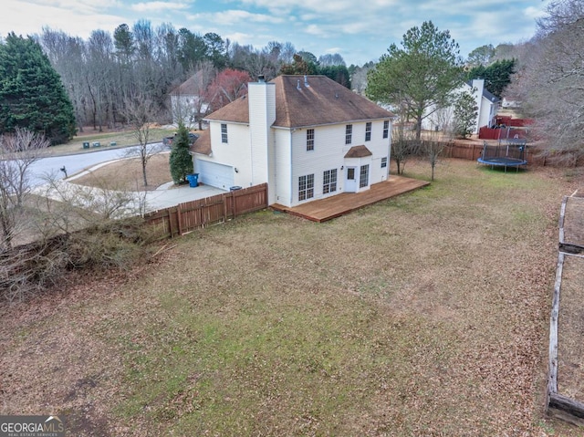 back of house with fence, a lawn, a wooden deck, a trampoline, and a chimney