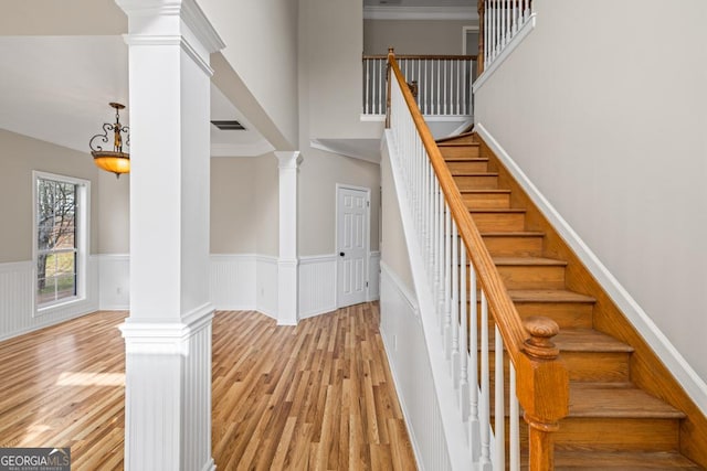 stairs with a wainscoted wall, wood finished floors, visible vents, decorative columns, and crown molding