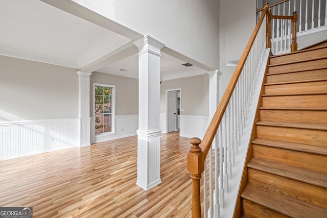 stairway featuring visible vents, ornamental molding, wainscoting, wood finished floors, and ornate columns