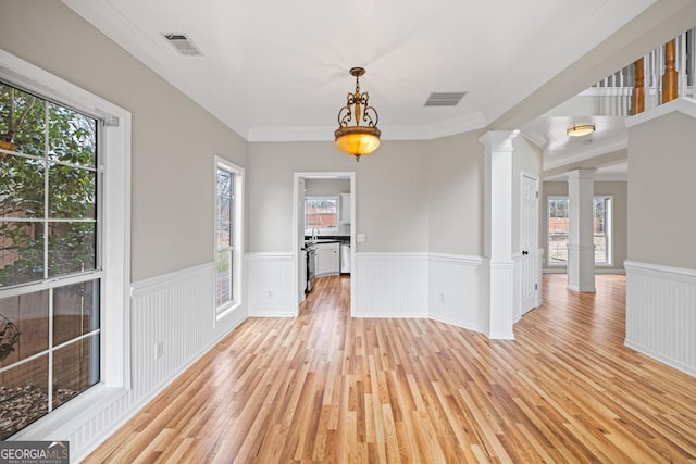 unfurnished dining area featuring ornate columns, visible vents, light wood-style floors, and wainscoting