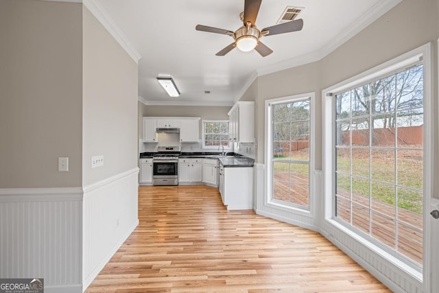 kitchen with a wainscoted wall, visible vents, white cabinets, dark countertops, and gas stove