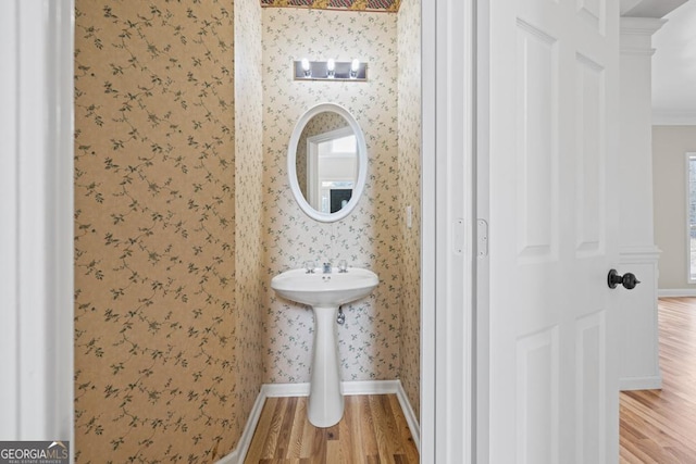 bathroom with ornamental molding, wood finished floors, baseboards, and wallpapered walls