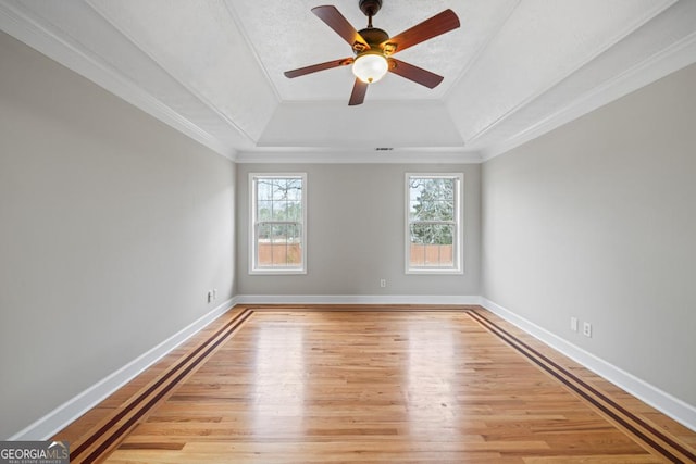 empty room featuring crown molding, wood finished floors, a raised ceiling, and baseboards