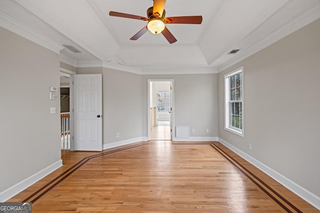 spare room featuring light wood finished floors, a tray ceiling, visible vents, and baseboards