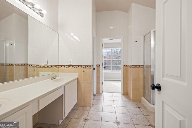 bathroom featuring double vanity, a stall shower, tile walls, tile patterned flooring, and a sink