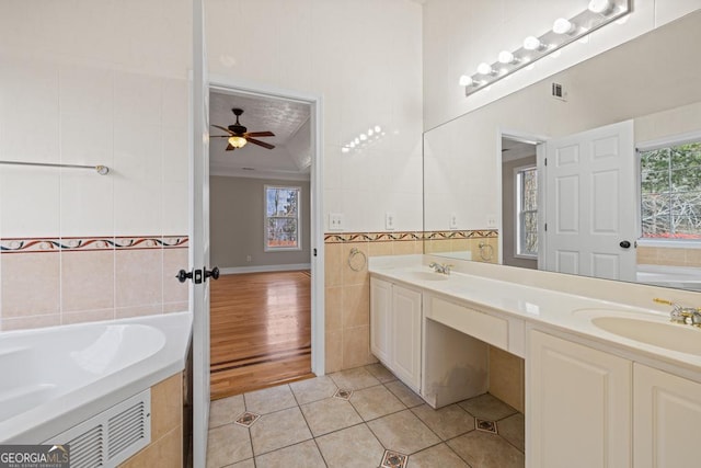 bathroom with a garden tub, tile walls, a wealth of natural light, a sink, and tile patterned floors