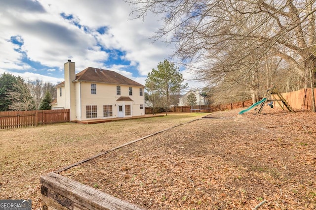 rear view of house featuring a fenced backyard, a chimney, and a playground