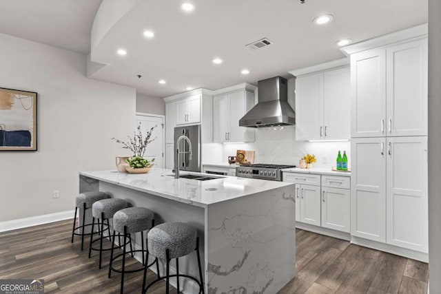 kitchen with visible vents, dark wood-style floors, a kitchen island with sink, wall chimney range hood, and a sink