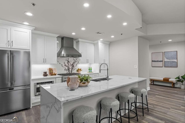 kitchen featuring visible vents, appliances with stainless steel finishes, wood finished floors, wall chimney range hood, and a sink