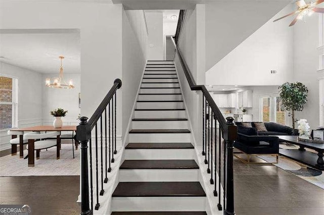 staircase featuring ceiling fan with notable chandelier, a high ceiling, visible vents, and a wealth of natural light