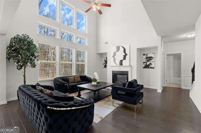 living area with dark wood-type flooring, plenty of natural light, a glass covered fireplace, and a ceiling fan