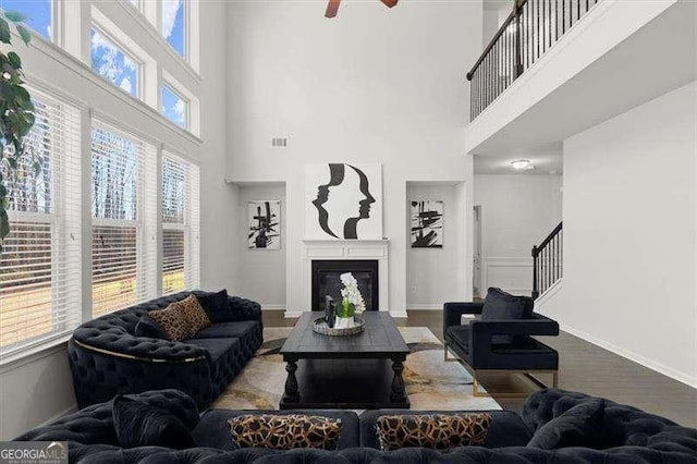 living area with a glass covered fireplace, visible vents, baseboards, and wood finished floors