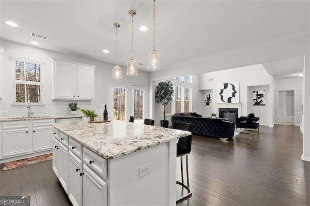 kitchen with decorative light fixtures, open floor plan, white cabinets, a kitchen island, and a kitchen bar