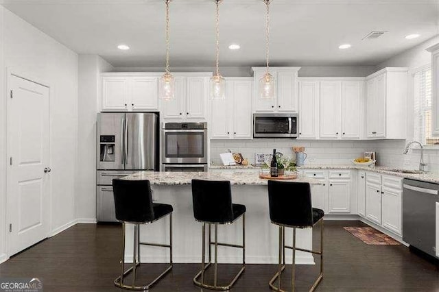 kitchen with a kitchen island, stainless steel appliances, white cabinetry, pendant lighting, and a sink