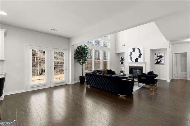 living area with visible vents, baseboards, dark wood-type flooring, and a glass covered fireplace