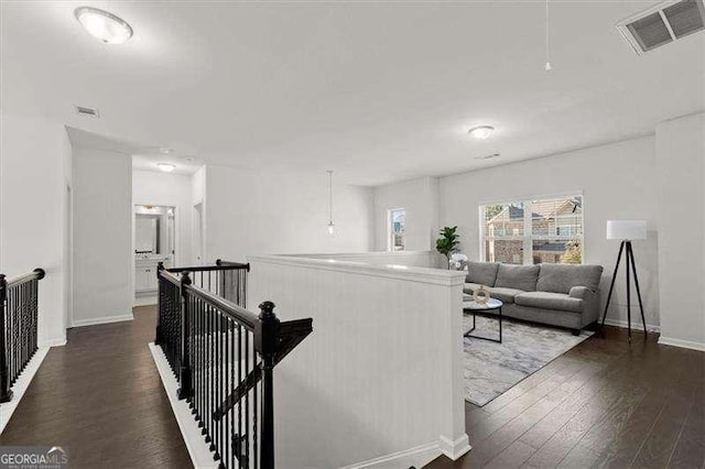 corridor featuring dark wood-style floors, baseboards, visible vents, and an upstairs landing