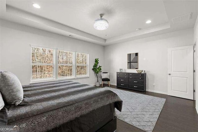 bedroom with baseboards, visible vents, dark wood-type flooring, a tray ceiling, and recessed lighting