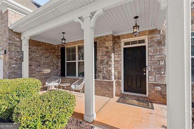 doorway to property featuring covered porch, stone siding, and brick siding