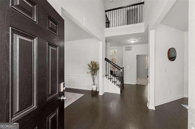 entrance foyer featuring visible vents, a wainscoted wall, dark wood-style flooring, stairs, and a decorative wall