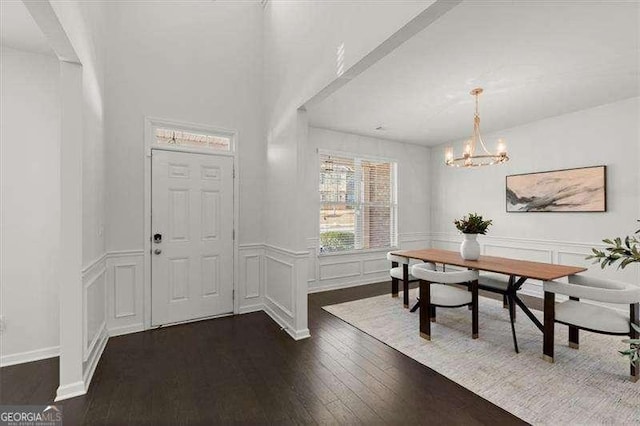 entrance foyer with dark wood-style floors, wainscoting, a decorative wall, and an inviting chandelier