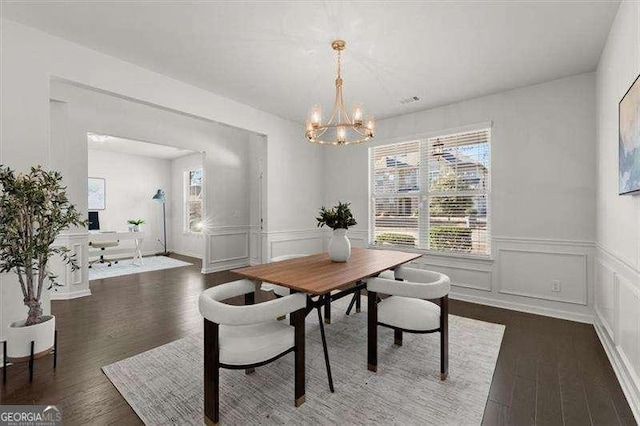 dining area featuring dark wood-type flooring, a wainscoted wall, a notable chandelier, and a decorative wall