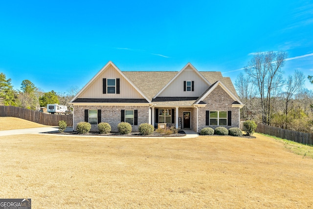 craftsman inspired home with roof with shingles, a front yard, fence, and brick siding