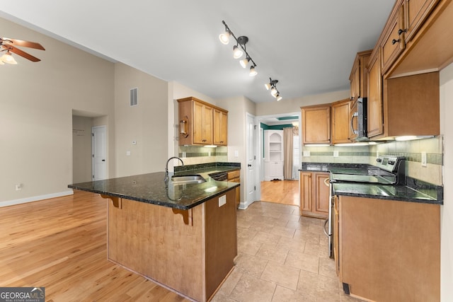 kitchen featuring stainless steel appliances, decorative backsplash, brown cabinetry, a sink, and a peninsula